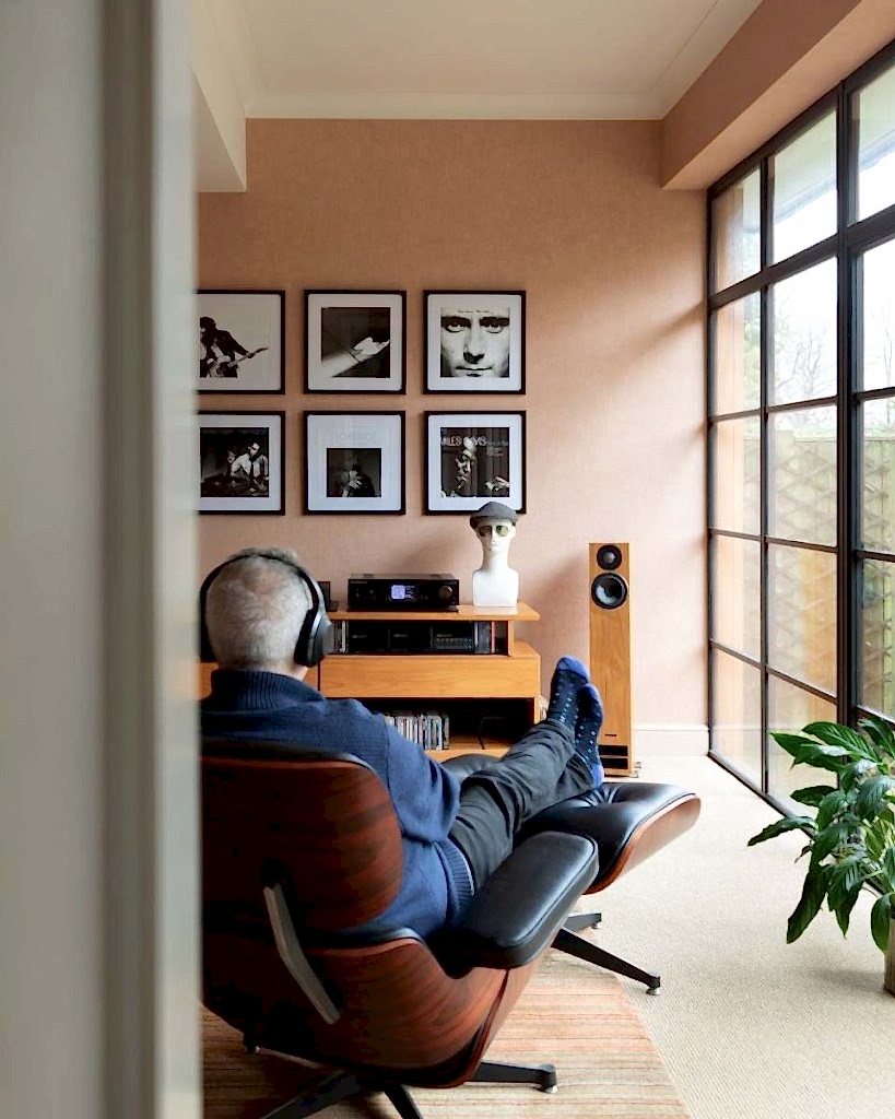 Modern listening room with lounge chair, high-end speakers, framed music artwork, and large industrial-style windows.