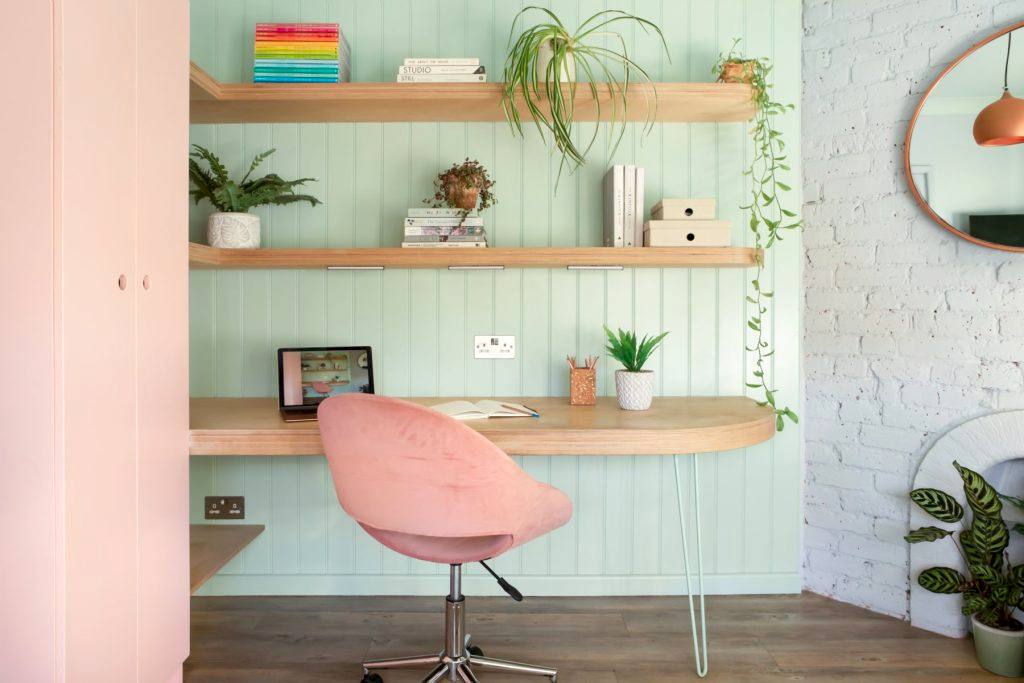 Soft-toned built-in shelving with books, decorative objects, and modern desk lamp beside blush cabinetry.