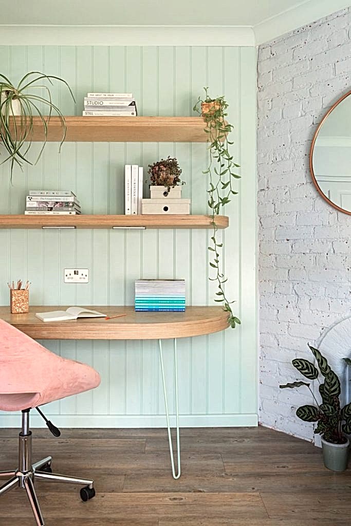 Soft-toned built-in shelving with books, decorative objects, and modern desk lamp beside blush cabinetry.