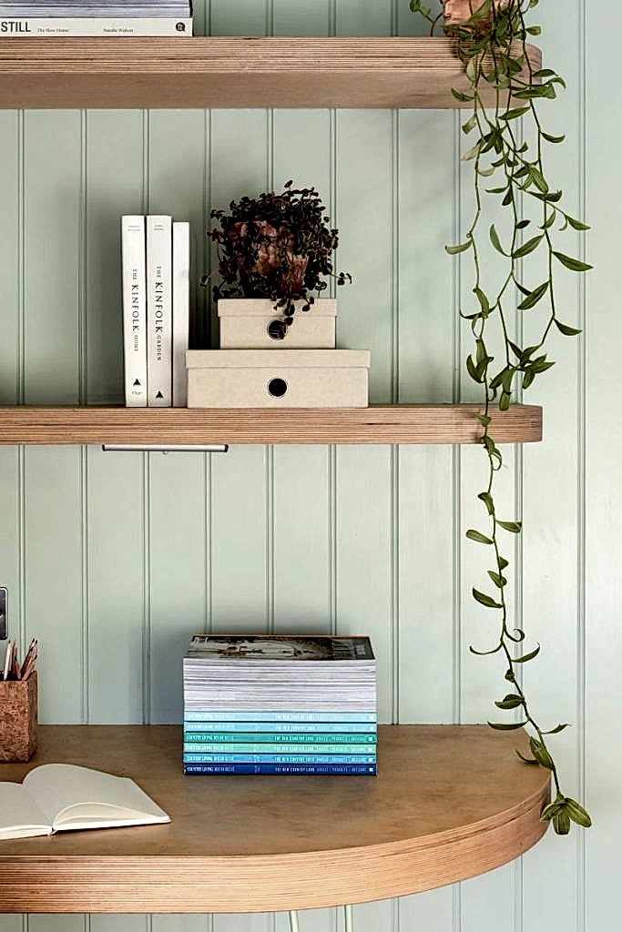 Soft-toned built-in shelving with books, decorative objects, and modern desk lamp beside blush cabinetry.