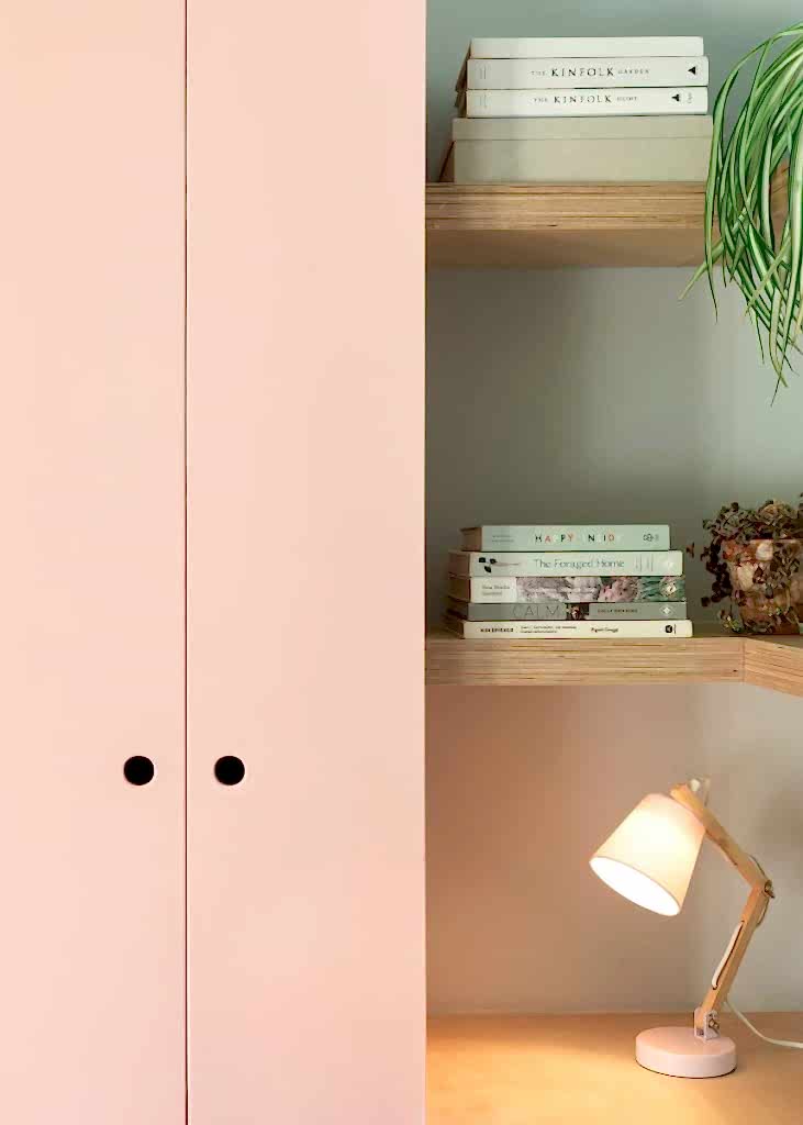 Soft-toned built-in shelving with books, decorative objects, and modern desk lamp beside blush cabinetry.