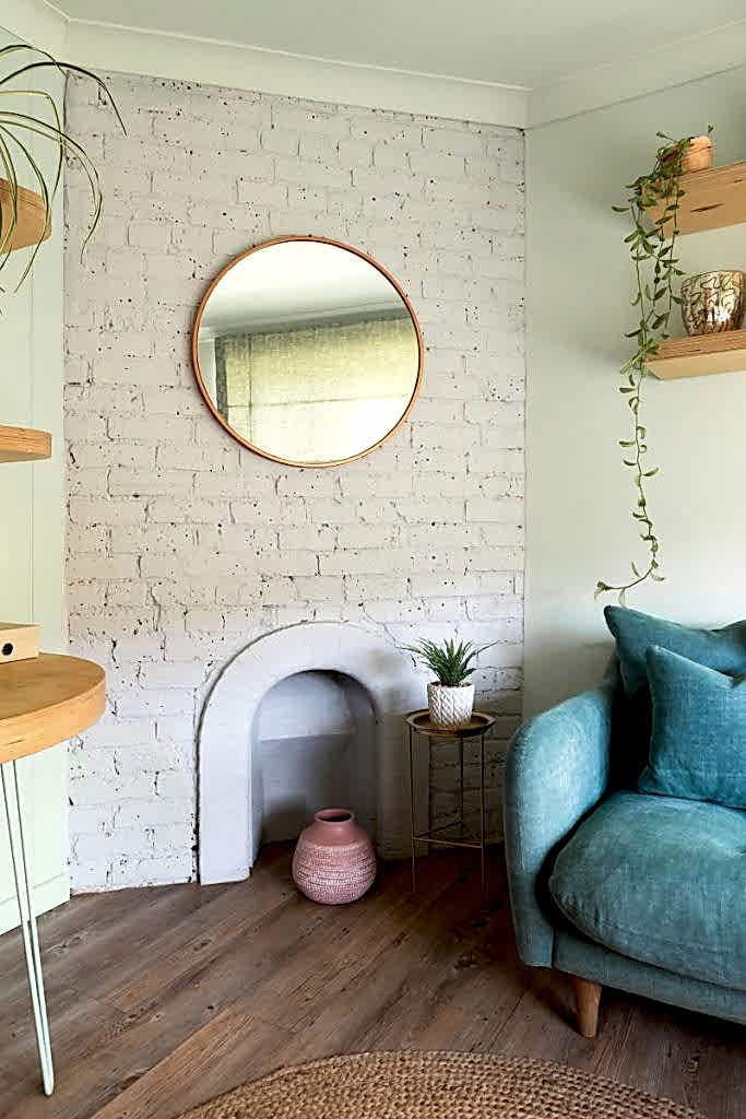 Styled lounge corner with decorative fireplace, round mirror, floating shelves and upholstered armchair.
