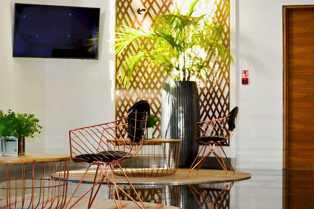 Modern office lounge area with copper wire chairs, wooden table, indoor plants, and contemporary styling