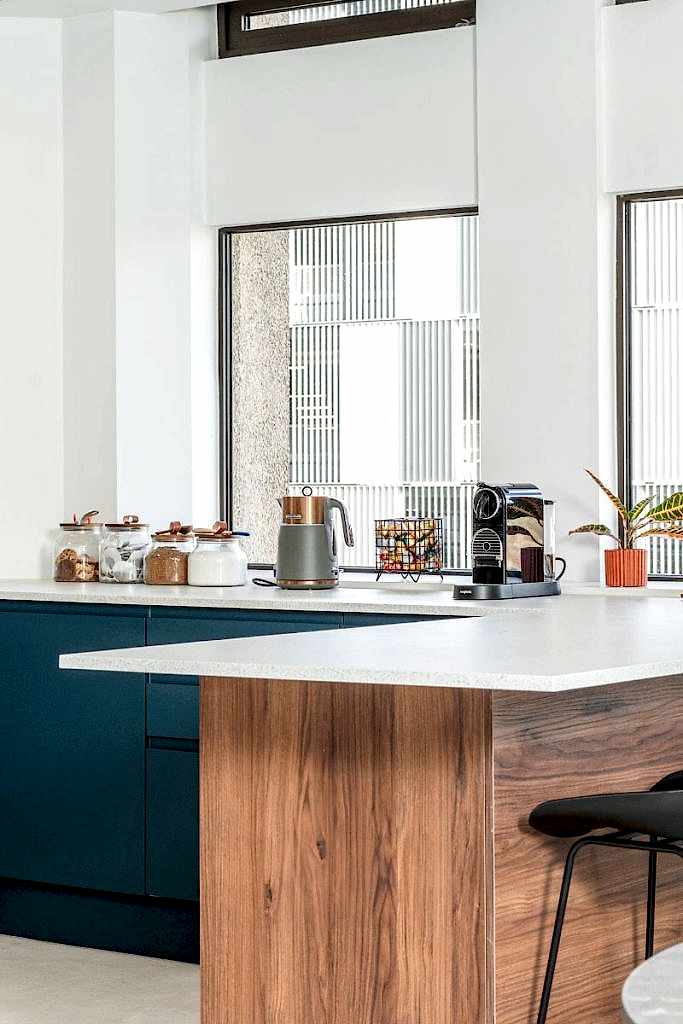 Modern office kitchenette with wooden island, blue cabinetry, coffee machine, and large windows.