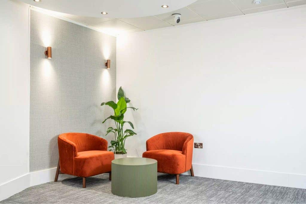 Office breakout seating with round wooden tables, orange chairs and indoor planting