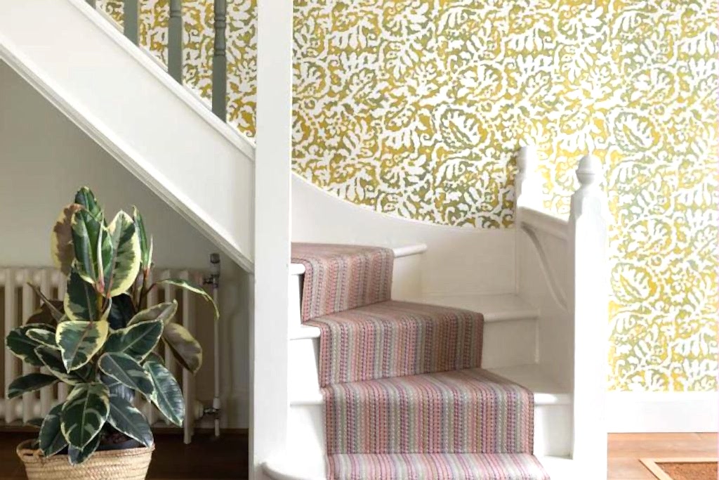 Contemporary staircase with patterned wallpaper, striped stair runner, white balustrade, and indoor plant.