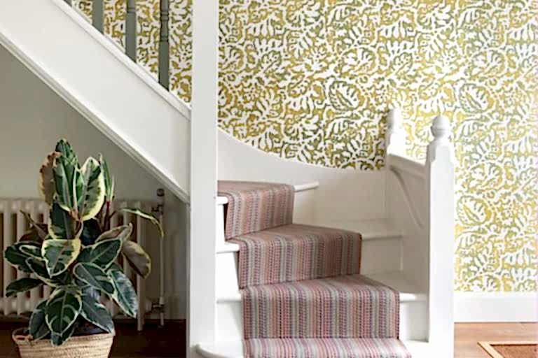 Contemporary staircase with patterned wallpaper, striped stair runner, white balustrade, and indoor plant.