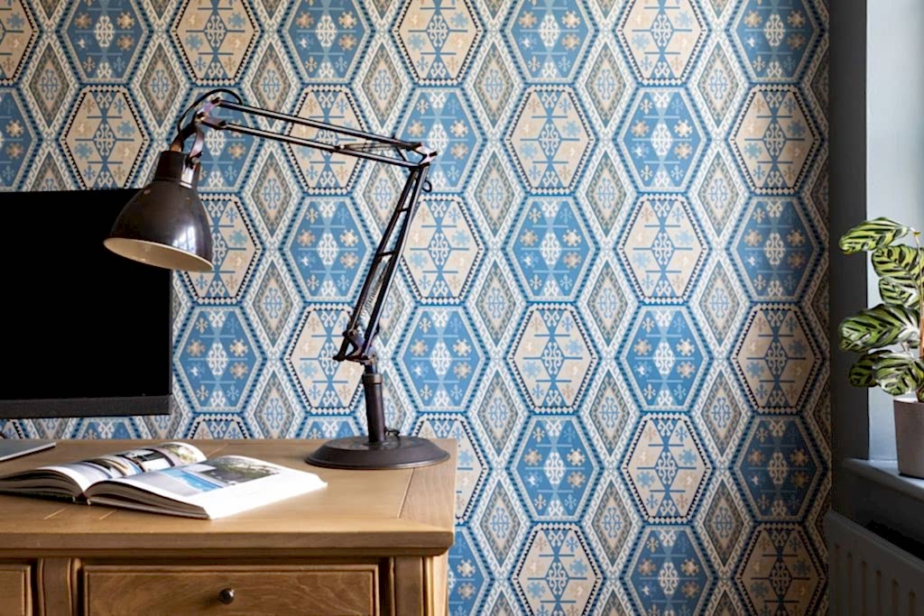 Contemporary home workspace with wooden desk, adjustable task lamp, patterned blue wallpaper, and modern styling.