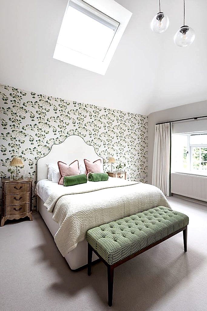 Bedroom with upholstered headboard, floral wallpaper, wooden bedside tables and layered cushions in soft pink and green tones.