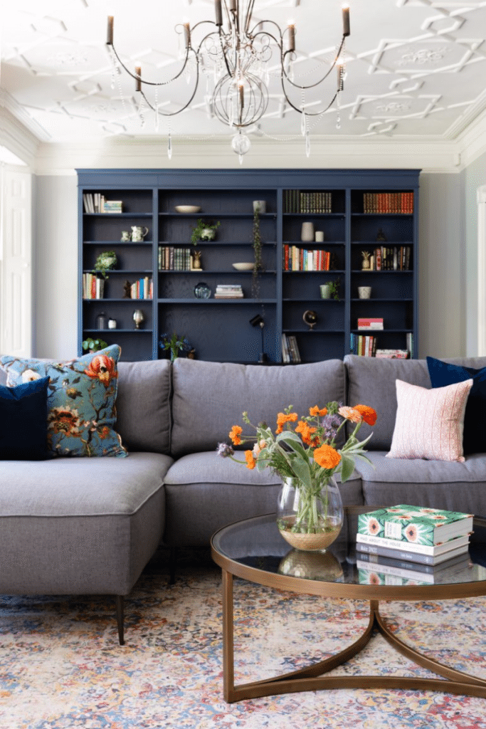Contemporary lounge with bespoke blue shelving, grey sectional sofa, and brass coffee table.