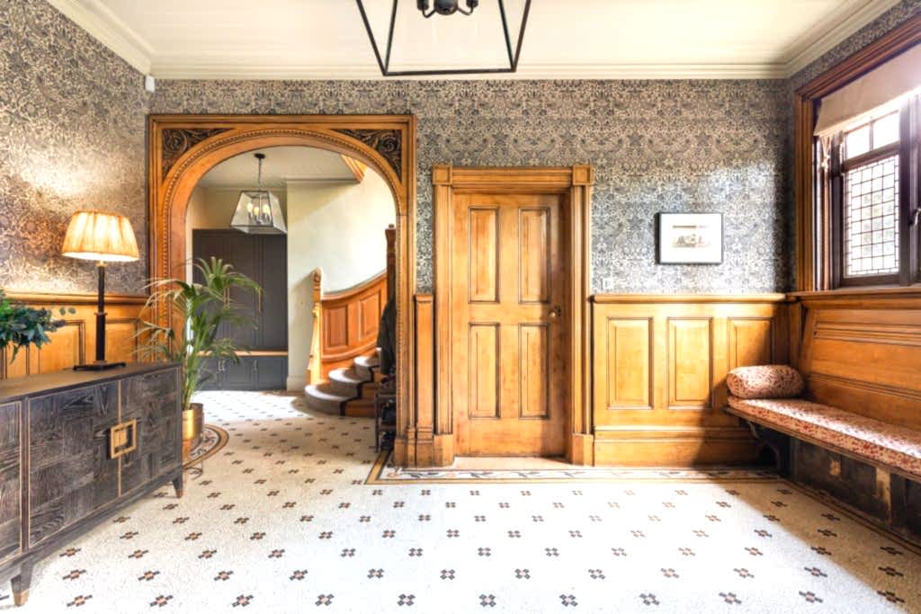 Period hallway featuring restored wooden panelling, decorative wallpaper, mosaic tiled flooring and an arched doorway leading to a staircase.